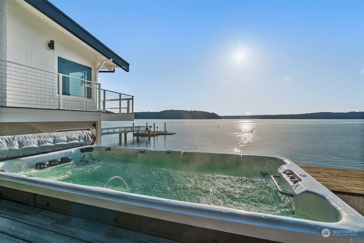 Big hot tub facing the ocean view. Next to it a large white house.